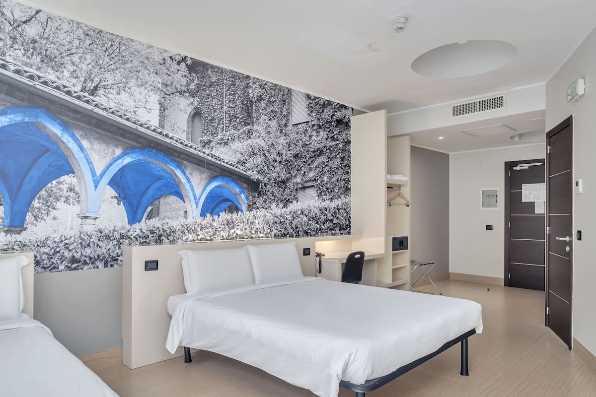 A modern hotel room with a large bed, a desk, and a wall-mounted TV.