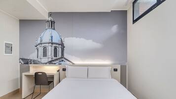 A hotel room with a bed, a desk, and a chair. There is a large wall mural of a building.
