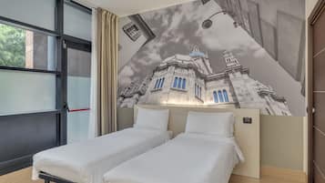 Une chambre d’hôtel avec deux lits simples, une grande fenêtre avec des rideaux et une fresque représentant un bâtiment sur le mur.