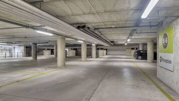 A spacious underground parking area with concrete pillars, fluorescent lighting, and a reception sign.