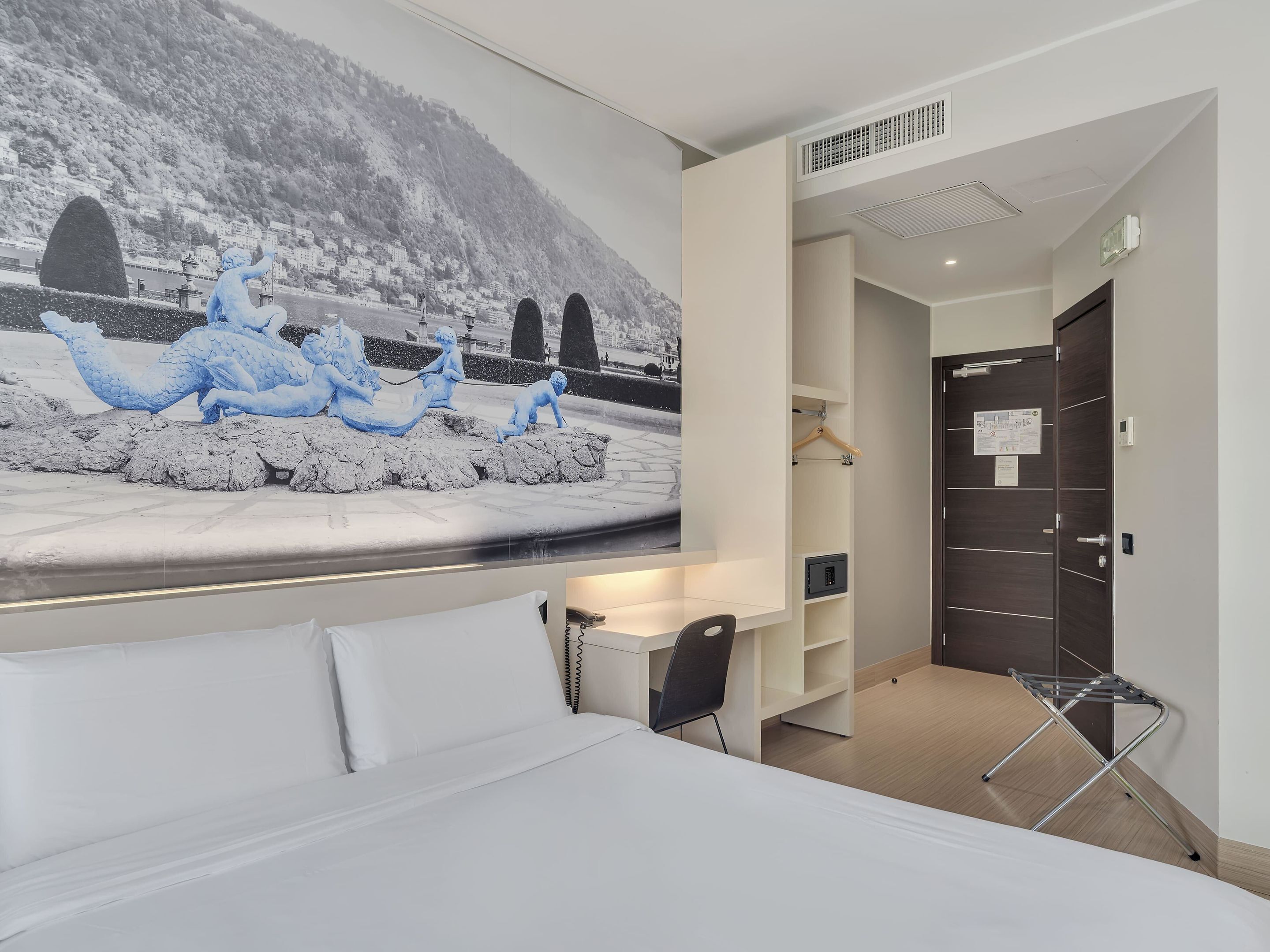 A hotel room with a bed, a desk, and a chair. There is a large mural on the wall depicting a snowy landscape with figures.