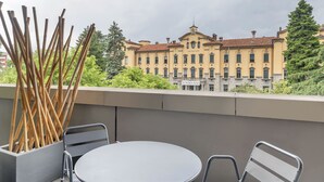 Ein Balkon mit rundem Tisch und zwei Stühlen, mit Blick auf ein historisches Gebäude, an dem das Schild "GIOVIO 100" angebracht ist.