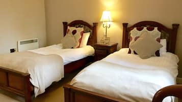 Two single beds with wooden headboards, a bedside table with a lamp, and a radiator on the wall.