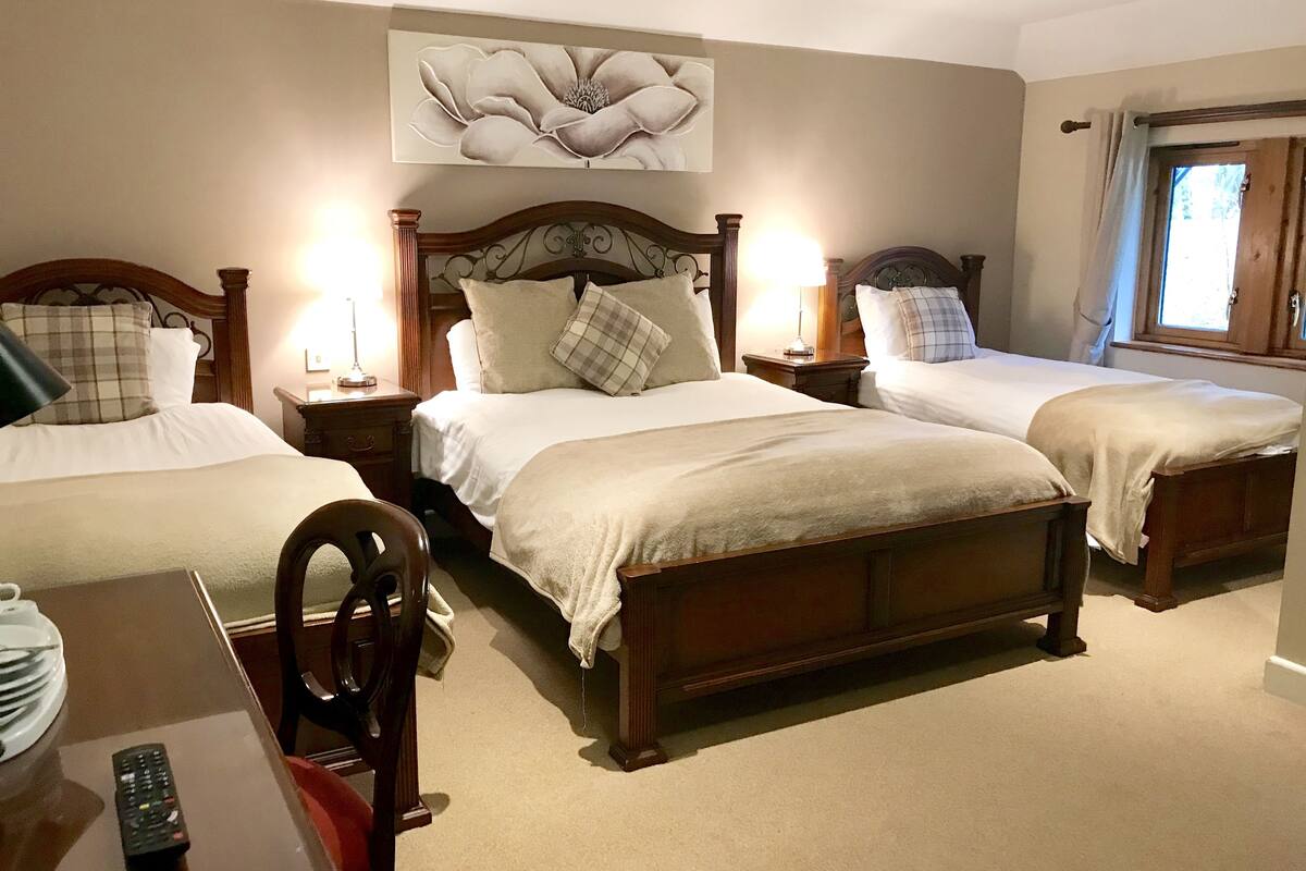 A hotel room with two single beds, a wooden headboard, a large floral artwork above the beds, and a window with curtains.