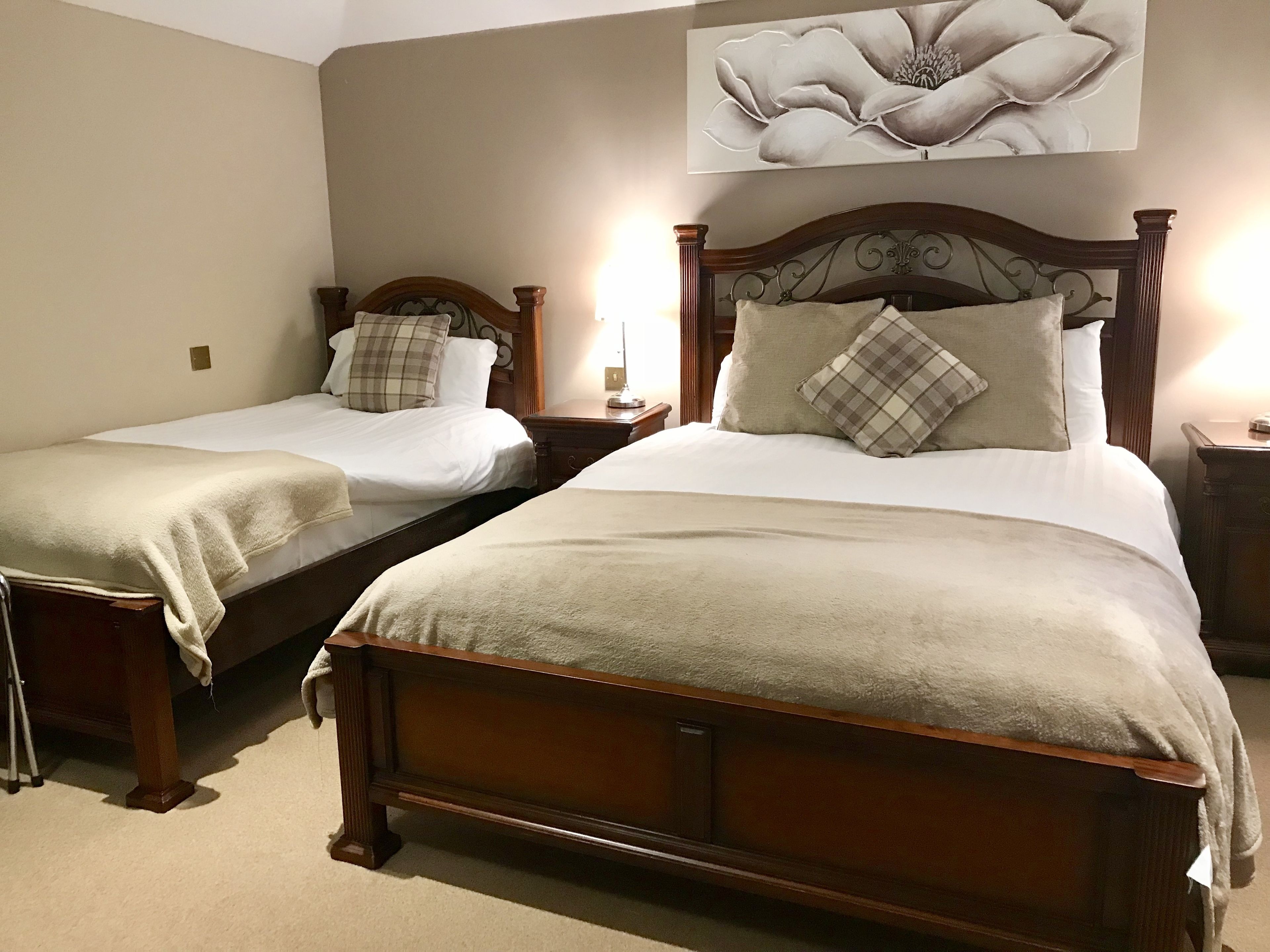 Habitación de hotel con dos camas individuales, cada una con cabecero de madera y mesita de noche. Se observa una obra de arte floral de gran tamaño en la pared sobre las camas.