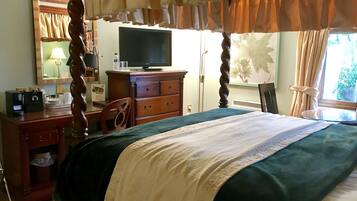 Habitación de hotel con cama con dosel, televisor sobre un aparador de madera, escritorio con lámpara y una silla.