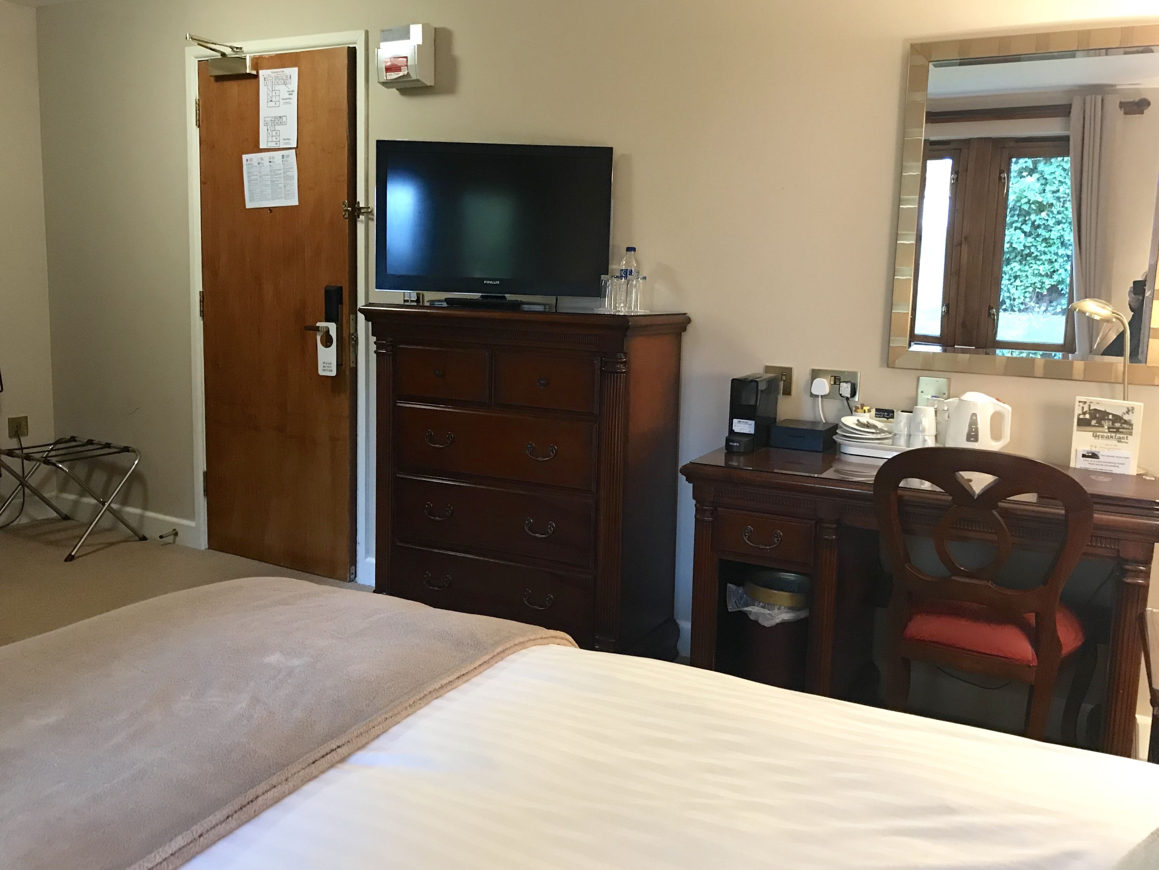 Una habitación de hotel con una cama, un aparador de madera, un escritorio con silla, un televisor y un espejo.