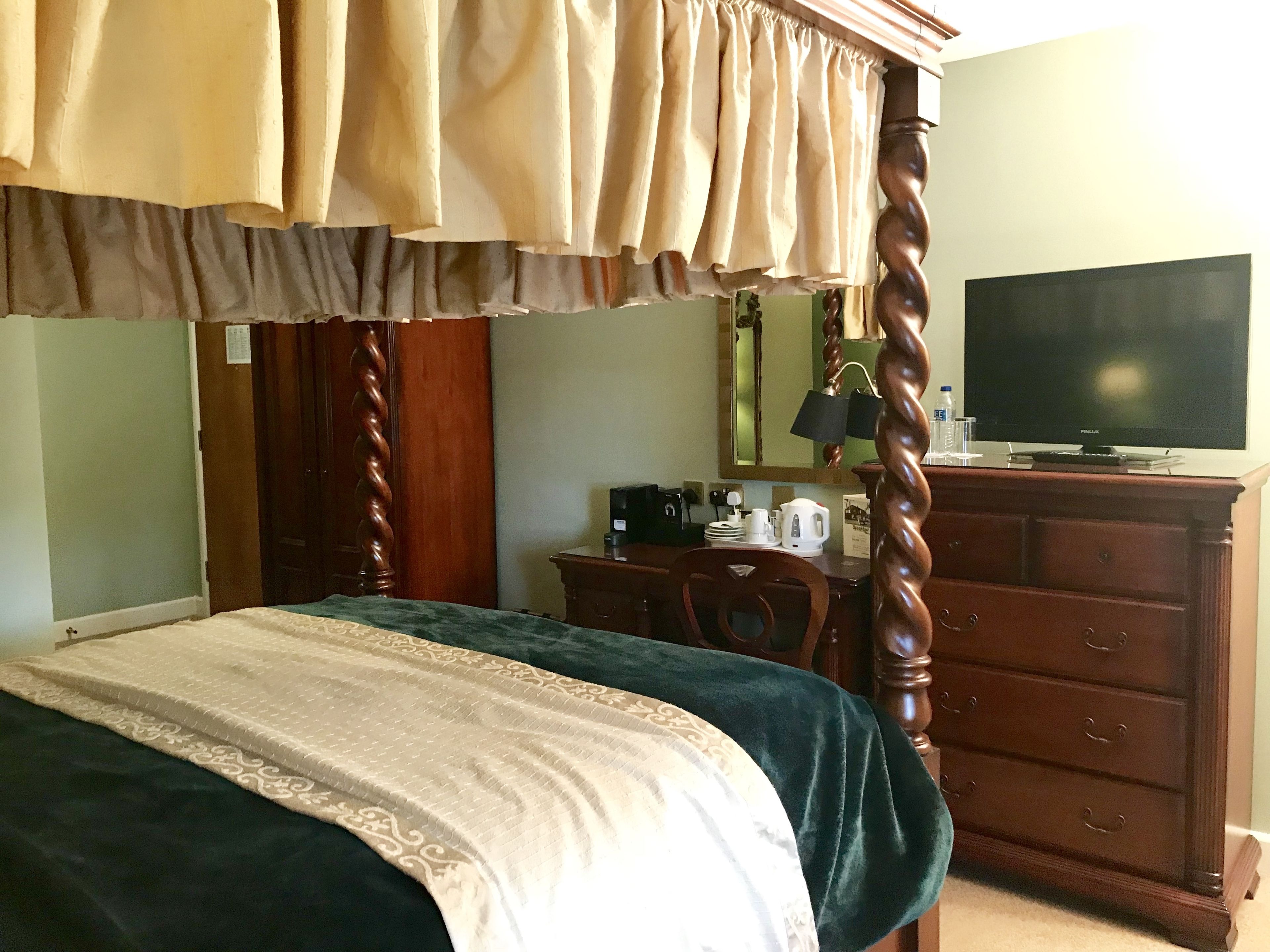 Une chambre à coucher avec un lit à baldaquin, une télévision, une commode et un bureau avec une lampe.