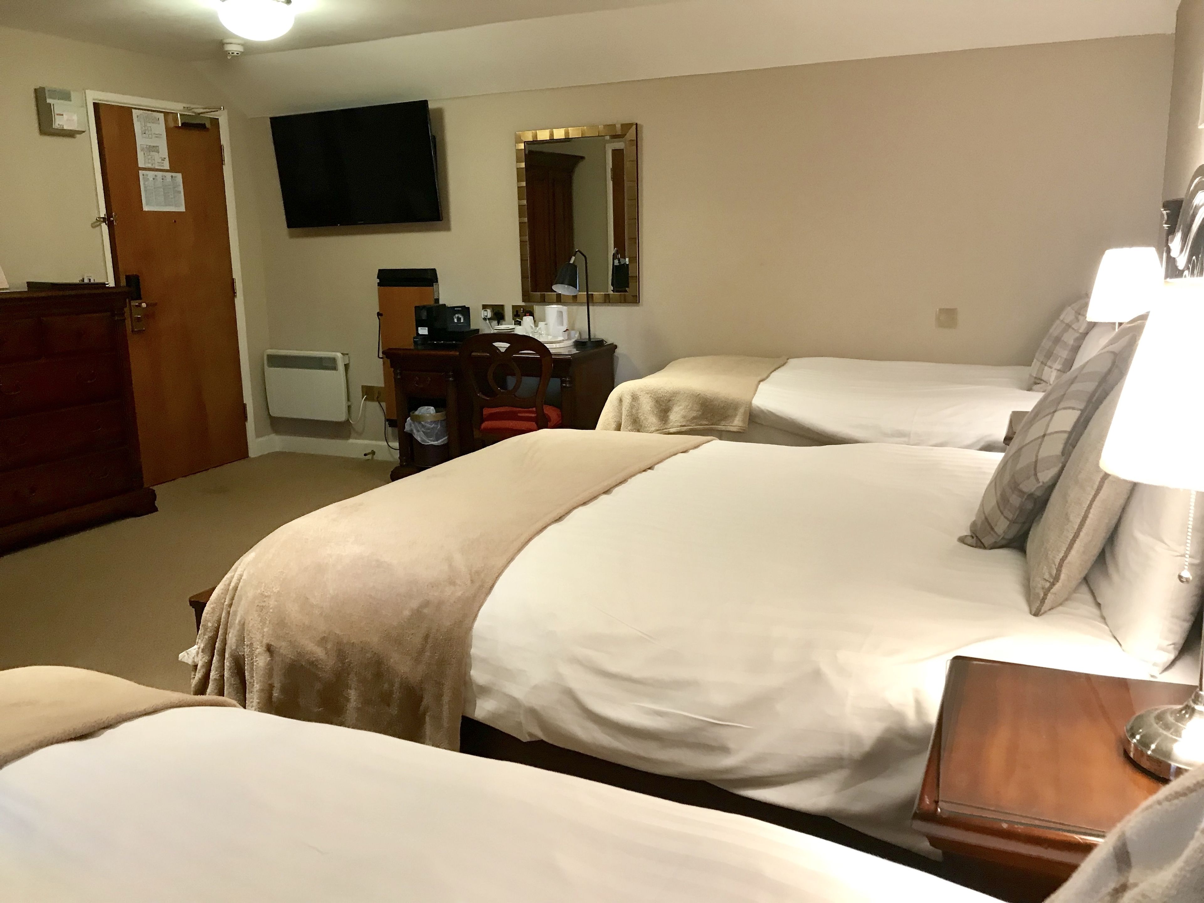 A hotel room with two beds, a desk, a chair, a TV, and a mirror.