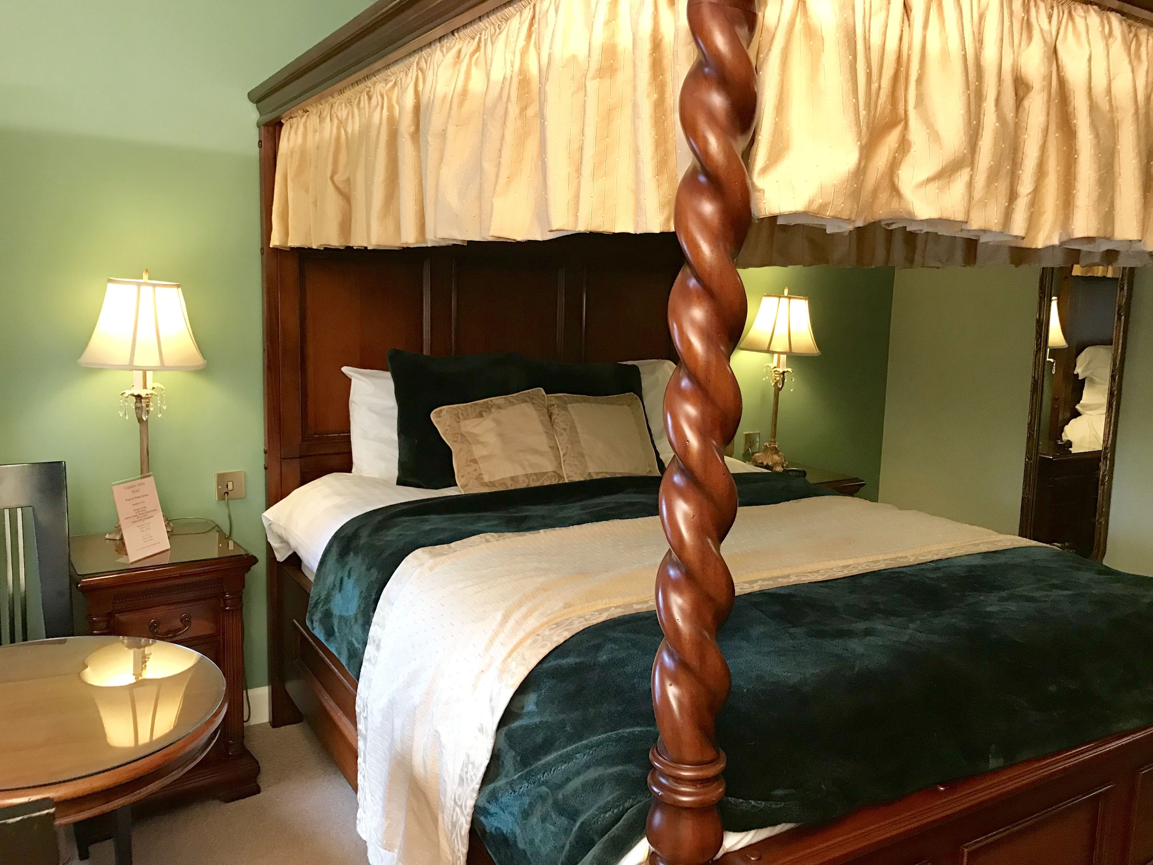 A four-poster bed with a dark green upholstered headboard, a cream-colored canopy, and two bedside lamps.