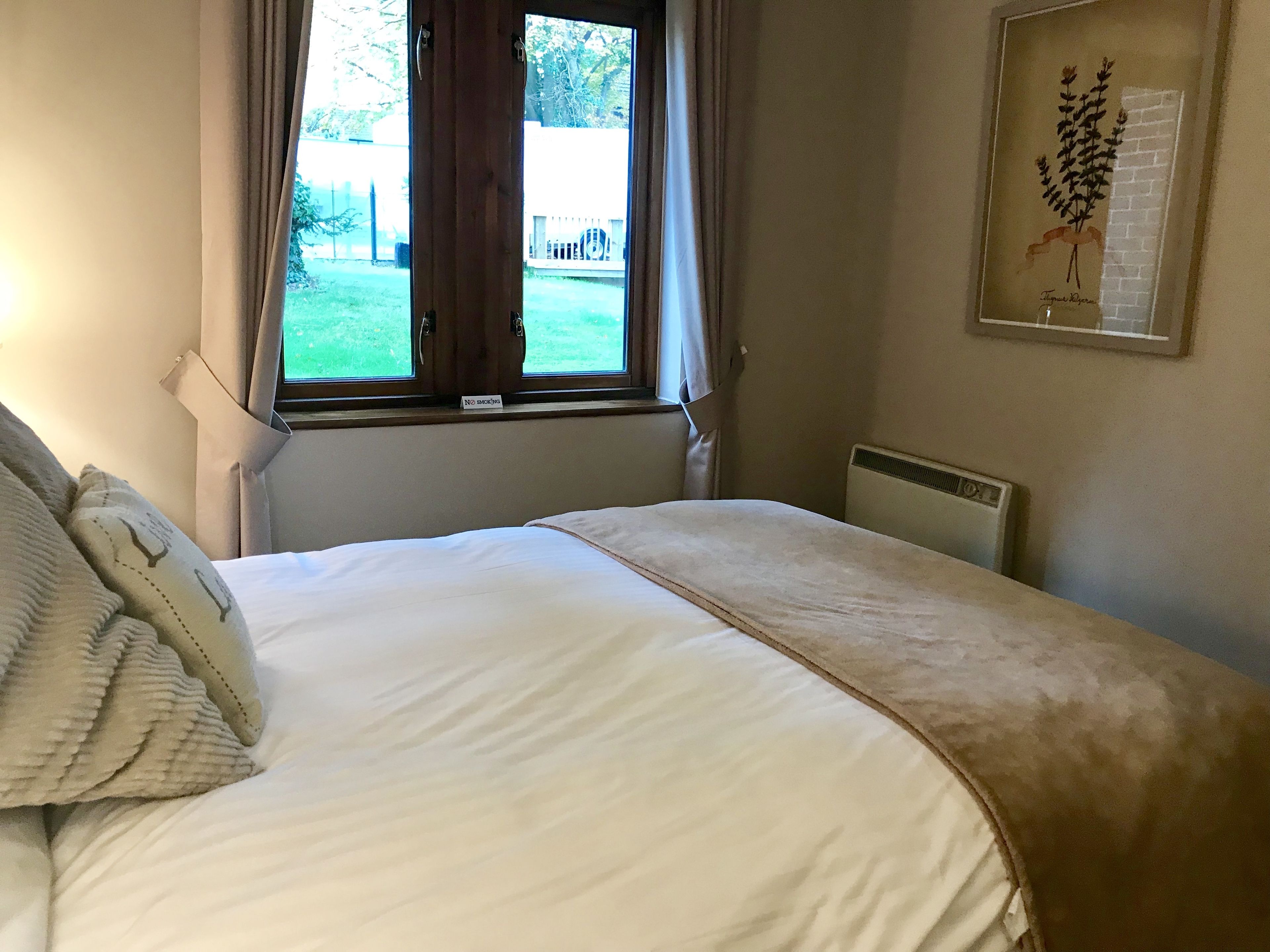A bedroom with a bed, a window with curtains, a radiator, and a framed botanical print on the wall.