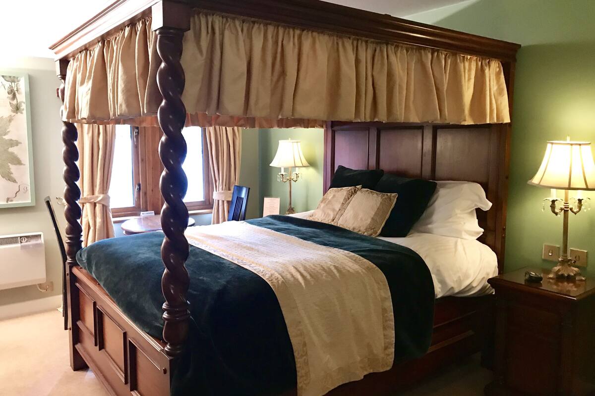 A four-poster bed with a canopy, a bedside table with a lamp, and a chair.