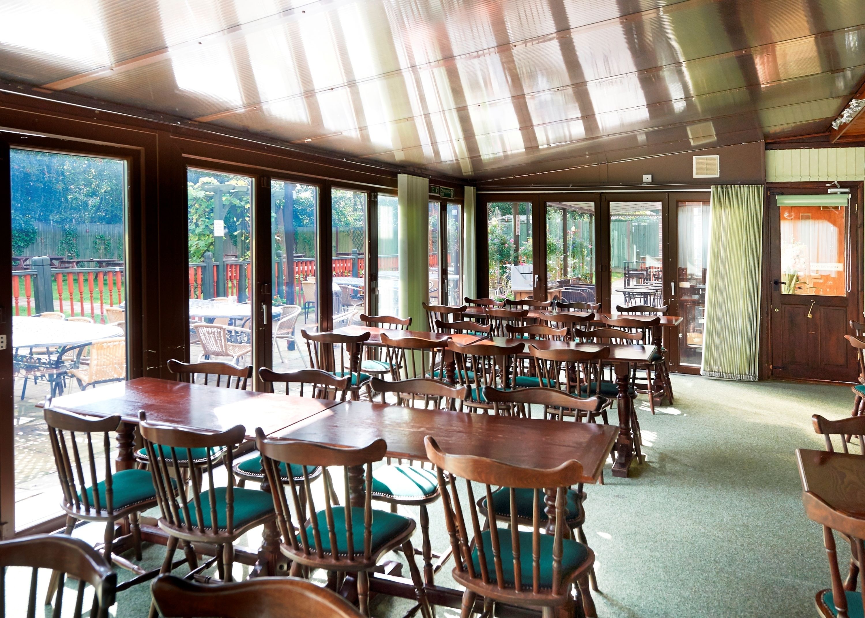 Een restaurant met houten tafels en stoelen, grote ramen en uitzicht op het terras.