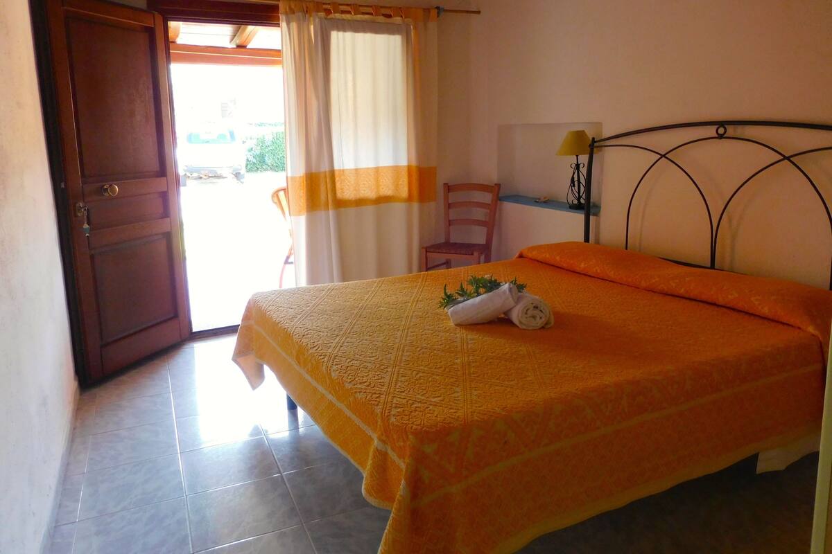 A bedroom with a bed, a chair, a lamp, and a door.