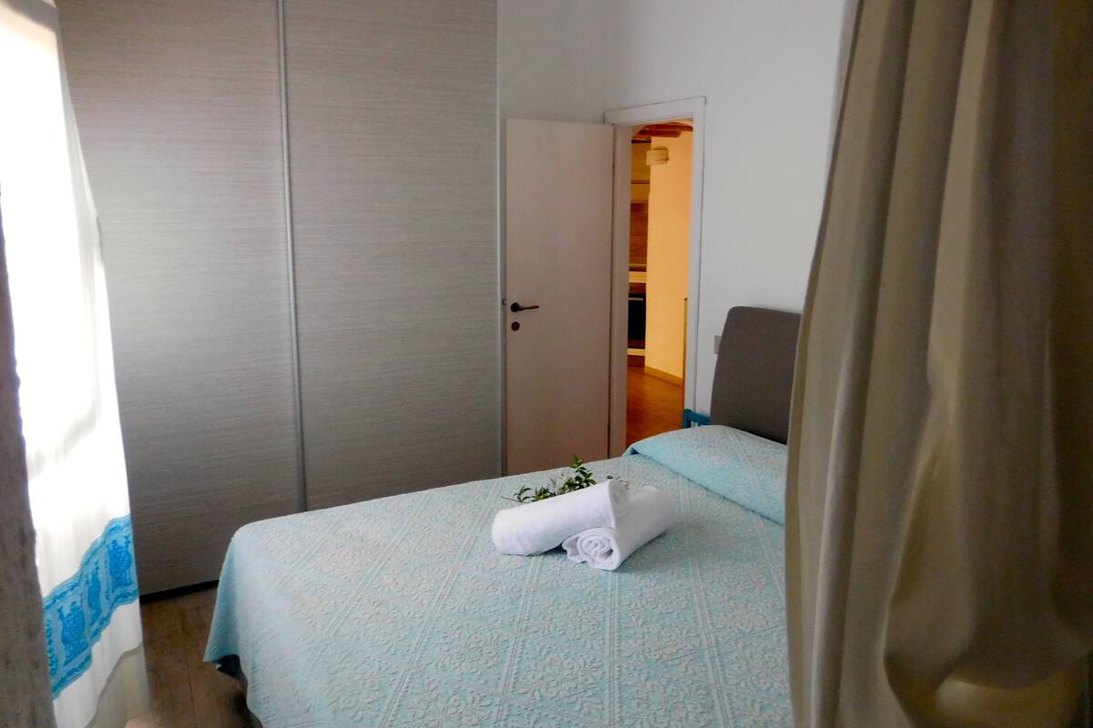 A hotel room with a bed, a chair, a wardrobe, and a door leading to another room.