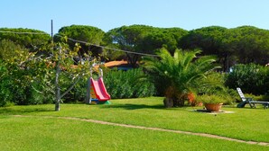 A grassy outdoor area with a playground featuring a red slide and a palm tree. - Residence La Pineta (Budoni)