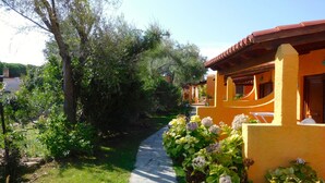 A pathway leading to a yellow building with a red roof, surrounded by greenery and a clear sky. - Residence La Pineta (Budoni)
