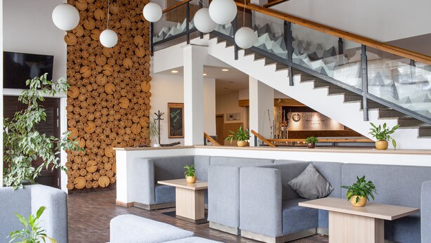 A modern interior with a wooden log wall, grey seating, and a staircase. - OREA Resort Devět Skal Vysočina (Snezne)