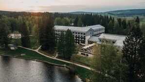 A modern building with a glass facade, surrounded by a forested area and a body of water. - OREA Resort Devět Skal Vysočina (Snezne)