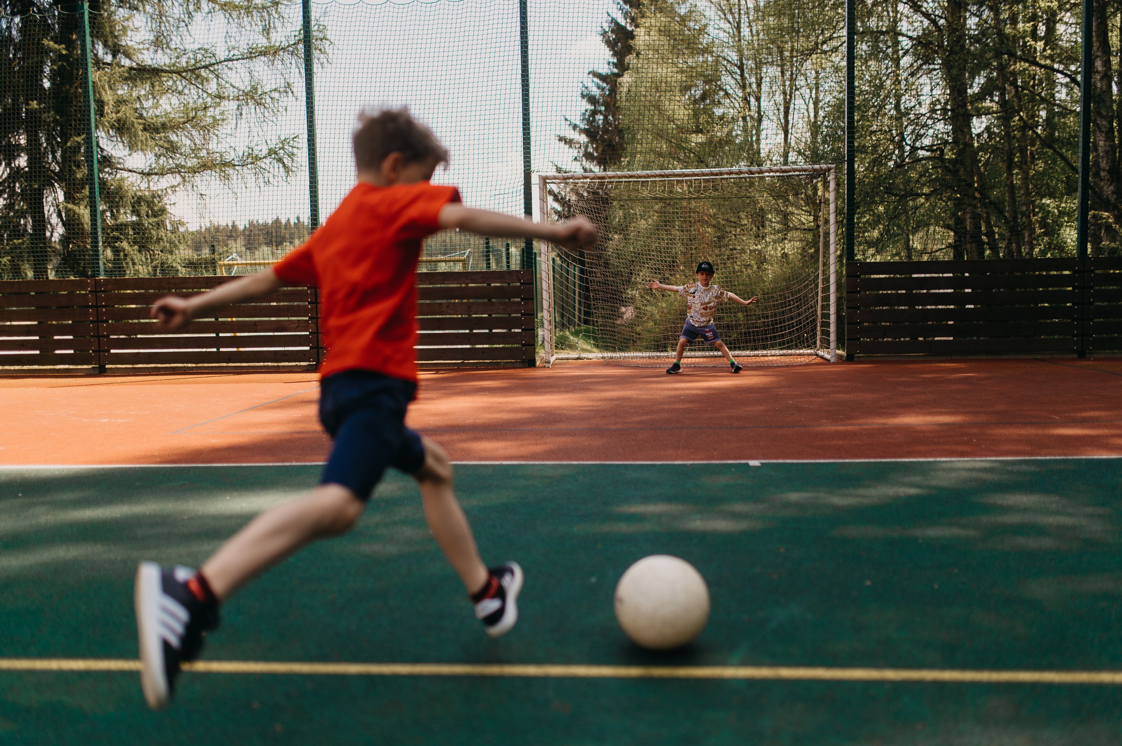 Una cancha de tenis con red, valla y árboles al fondo.