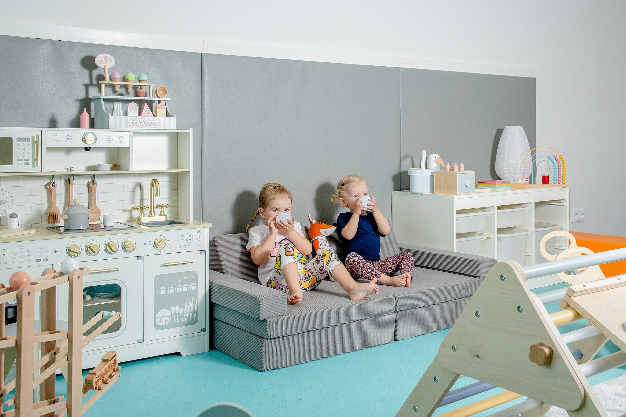 A children's playroom with a play kitchen, seating area, and storage units.