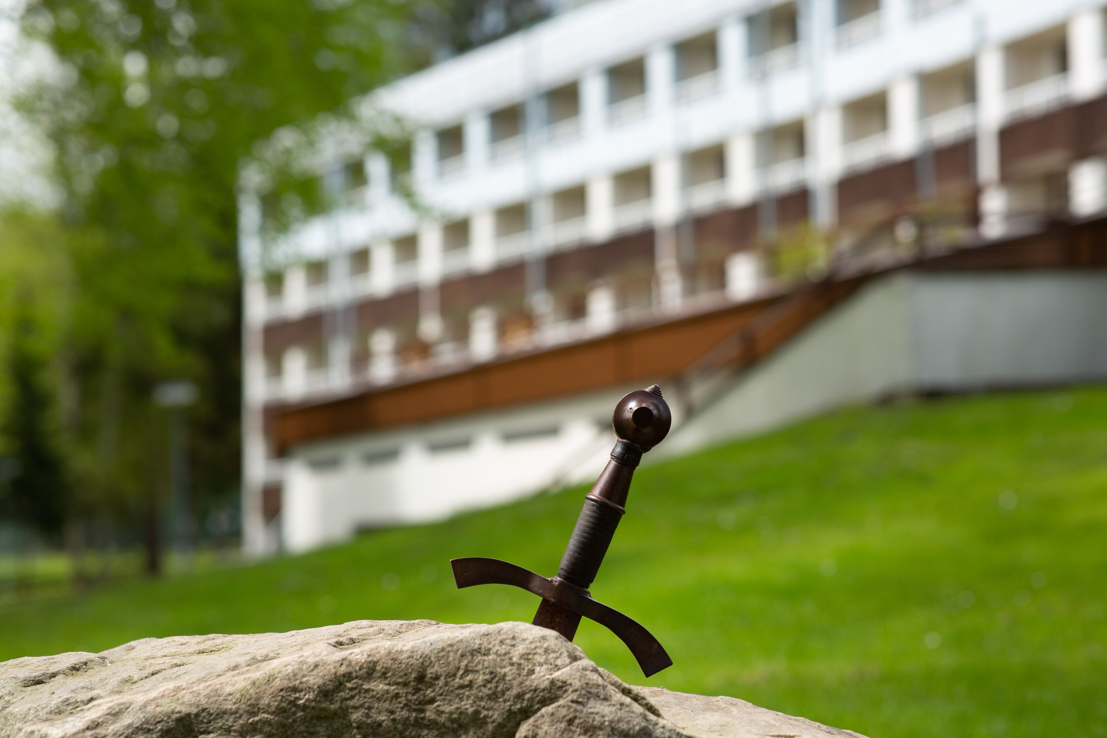 A sword on a rock with a building in the background.