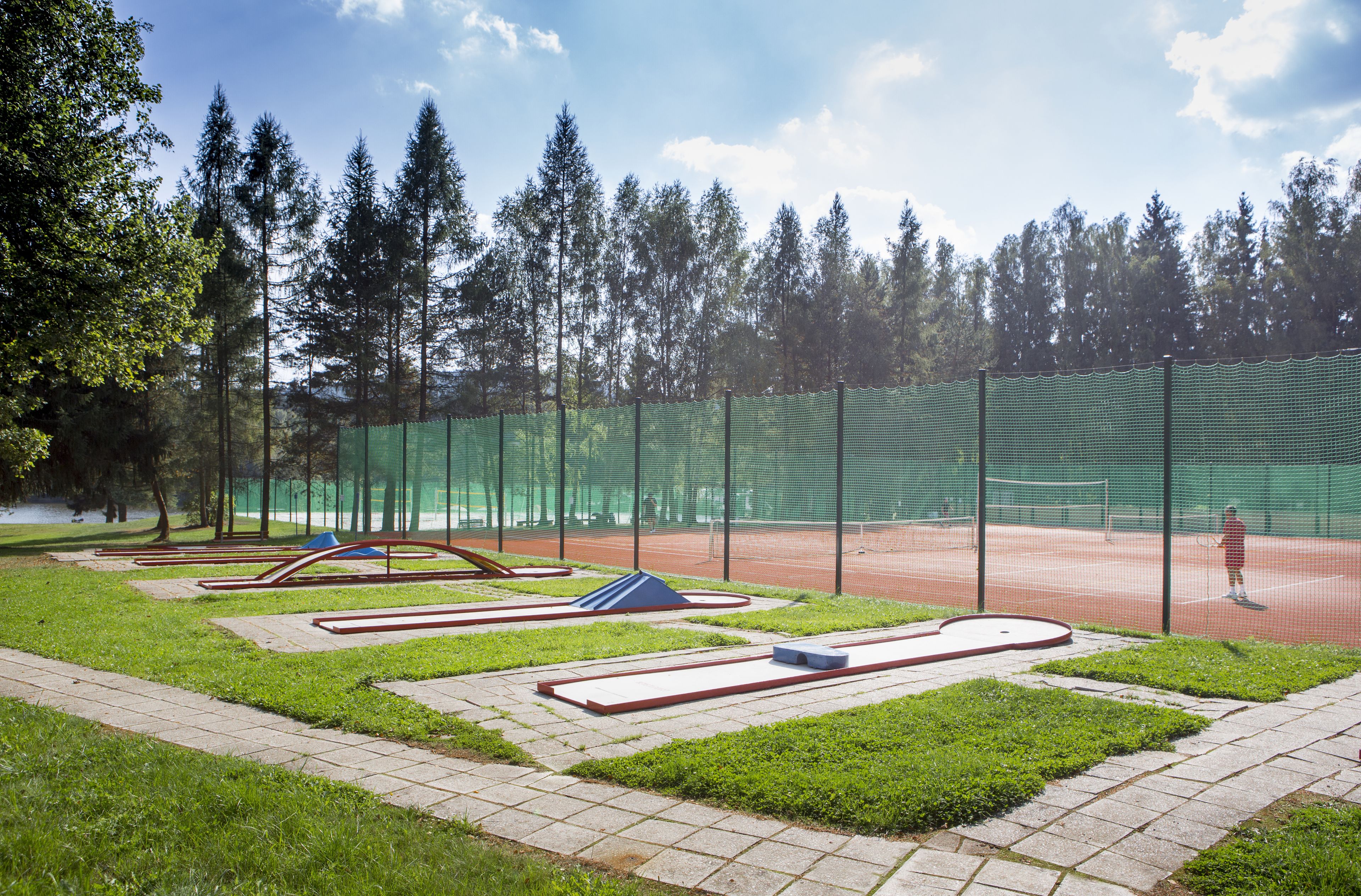 Tenniskenttä, jossa on verkko, ja jonka ympärillä on vihreä aita ja puita.