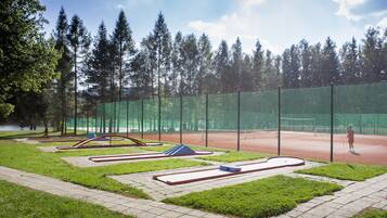 Tenniskenttä, jossa on verkko, ja jonka ympärillä on vihreä aita ja puita.
