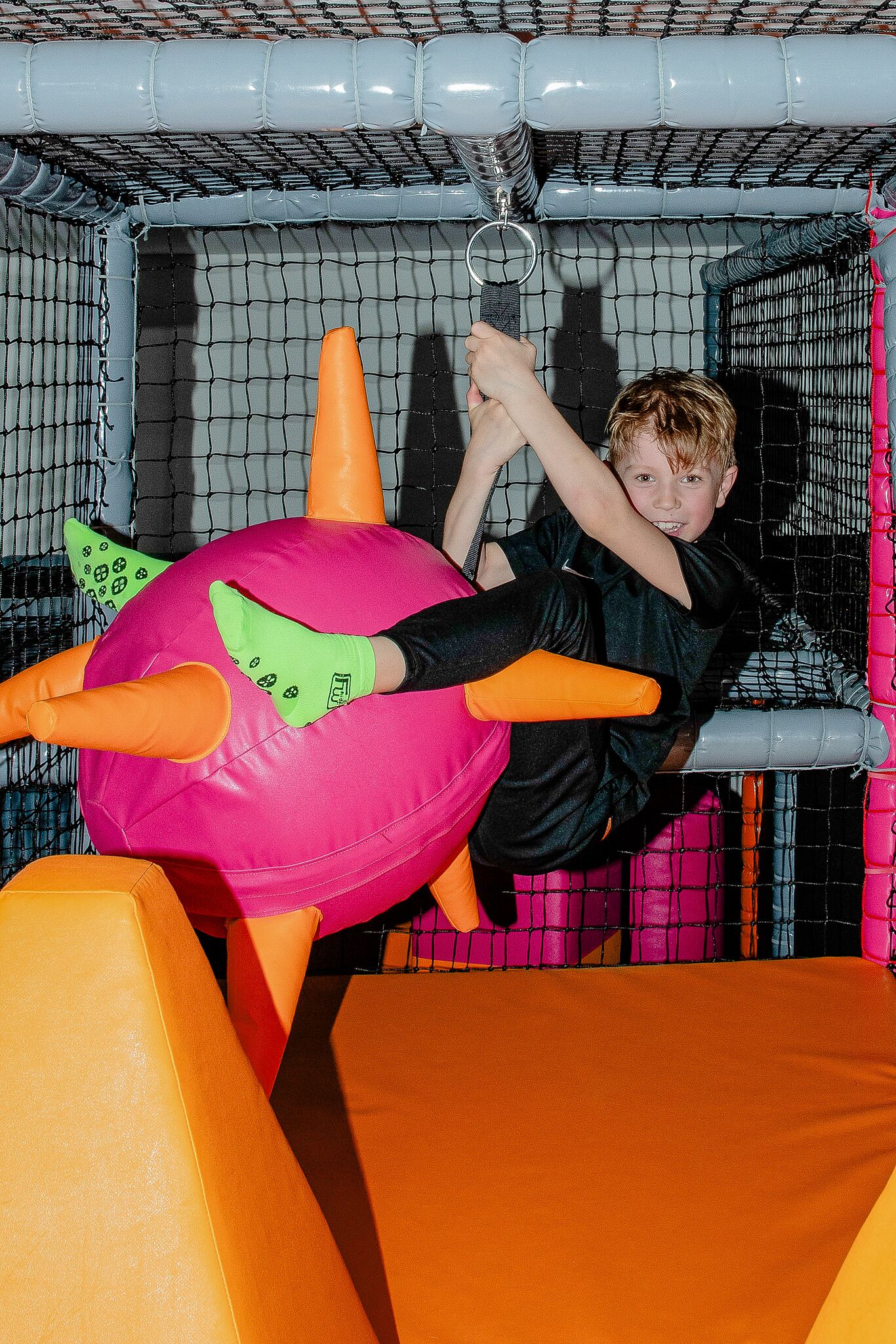A child playing in a netted play area with a large inflatable ball and orange padding.