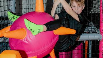 A child playing in a netted play area with a large inflatable ball and orange padding.