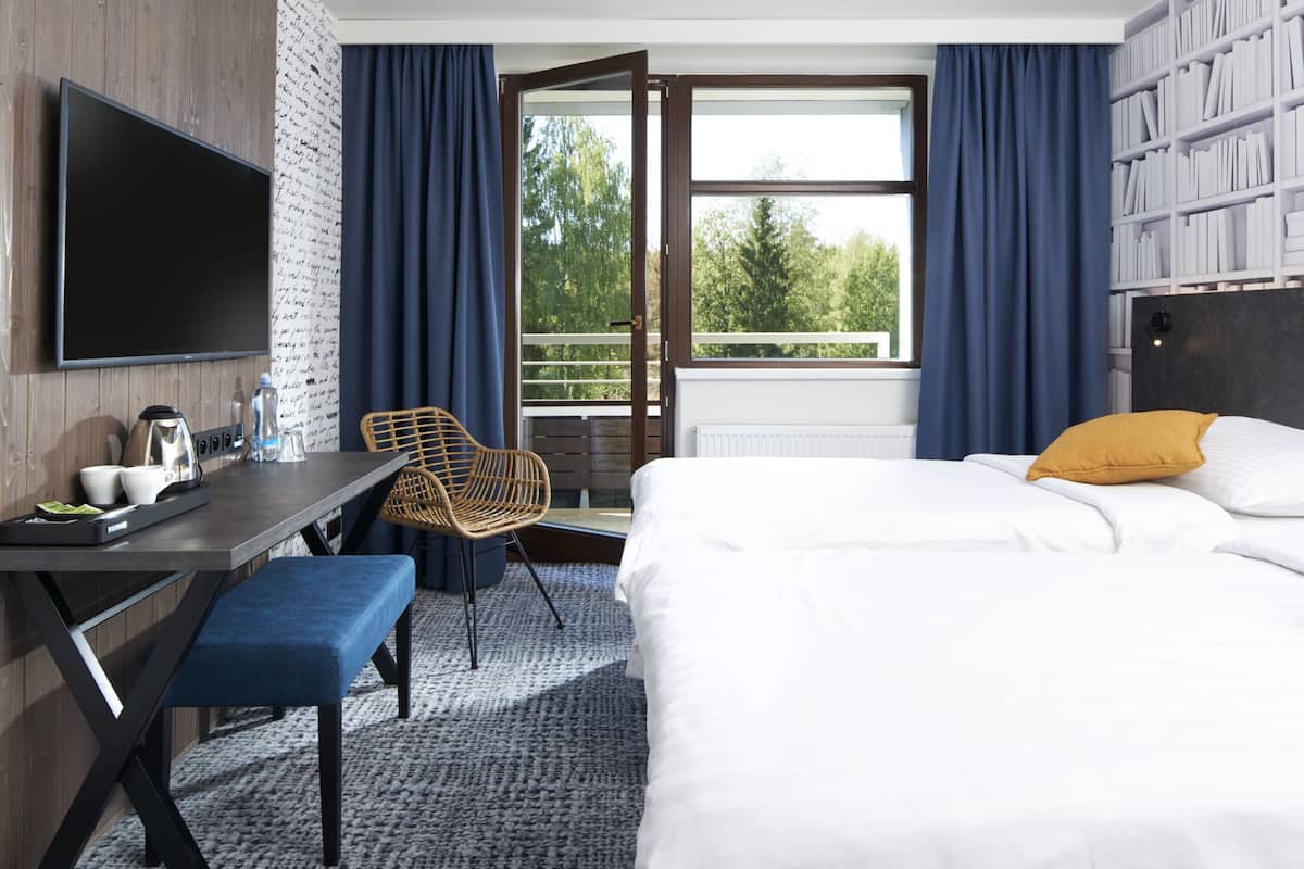 A hotel room with a bed, a desk with a chair, a television, and a bookshelf.