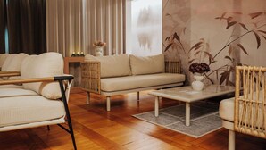 A modern living room with a sofa, chairs, a coffee table, and a large window with a view of a forest. - OREA Resort Devět Skal Vysočina (Snezne)