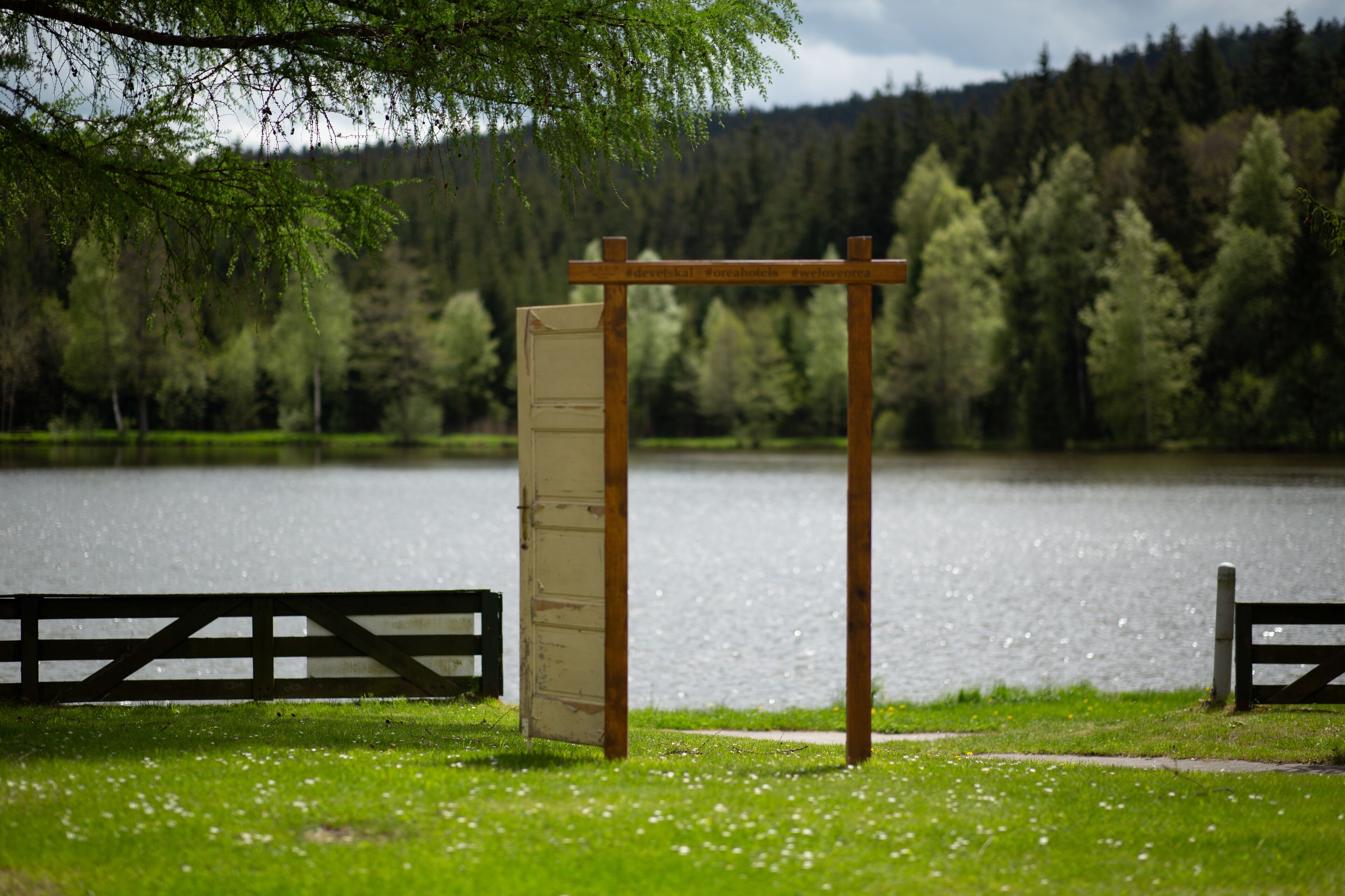 En pergola av trä med en vit panel i en park vid en sjö.