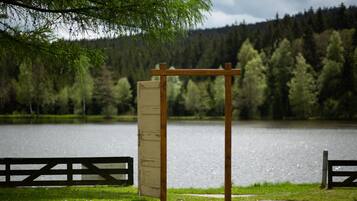 En pergola av trä med en vit panel i en park vid en sjö.