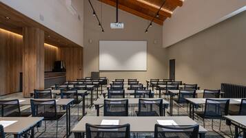 Un salón de conferencias con varias mesas y sillas, una pantalla grande y techo de madera.