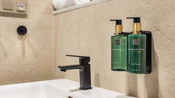 Un baño con lavamanos blanco, grifo negro y dos botellas verdes de jabón de manos y loción corporal Rituals of Jing.