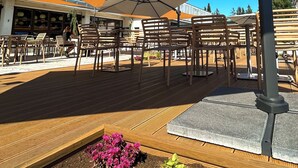 An outdoor seating area with wooden chairs and tables, umbrellas, and a garden with various plants. - OREA Resort Devět Skal Vysočina (Snezne)