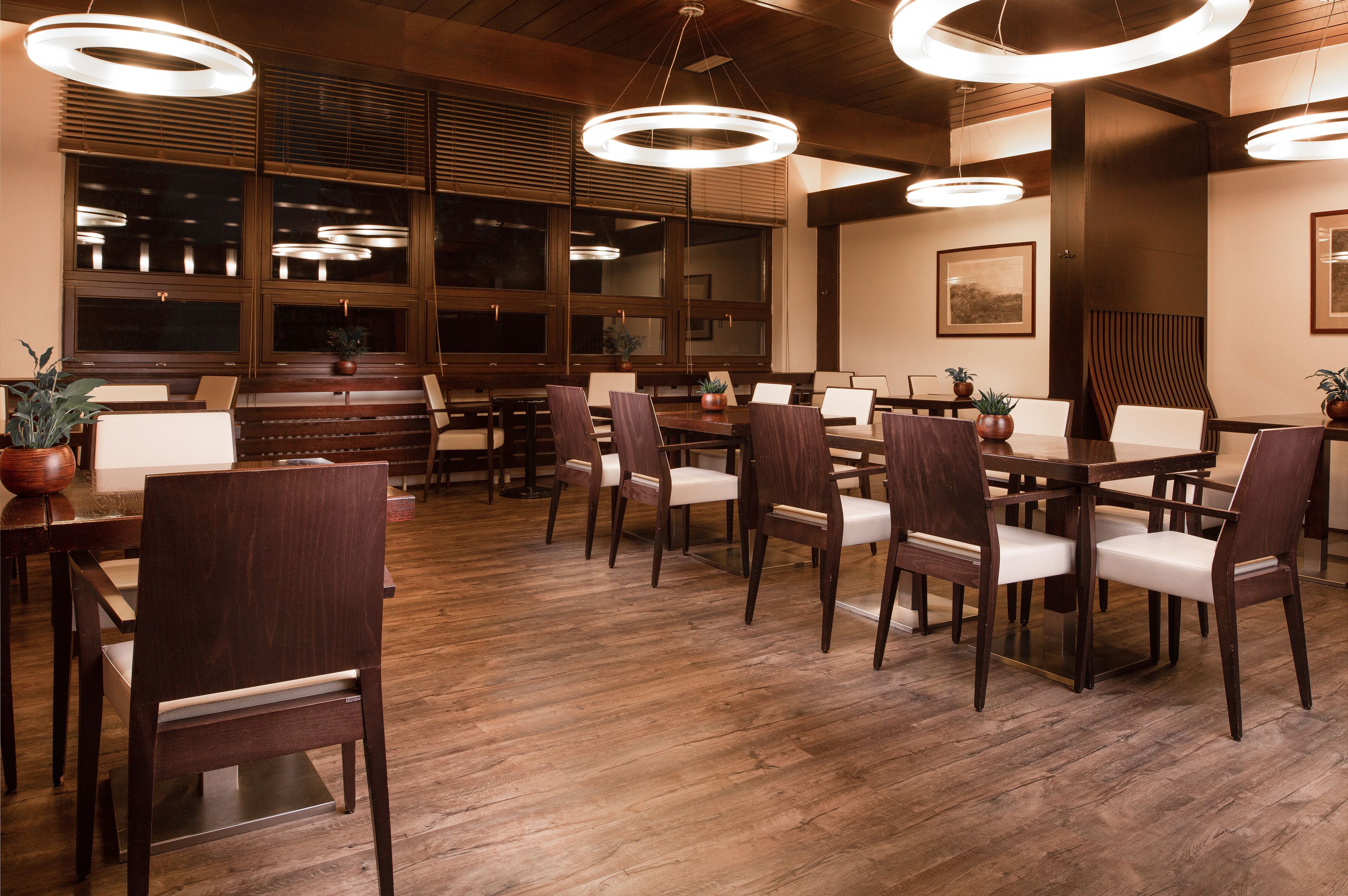 Un restaurante con suelo de madera, mesas y sillas de madera oscura, y lámparas colgantes circulares.