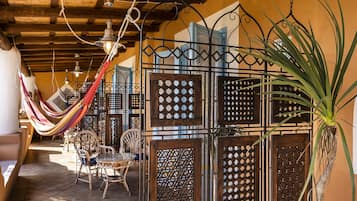 Cómodo espacio exterior con sillas de mimbre y una hamaca, rodeado de paneles de madera decorativos y una planta grande.