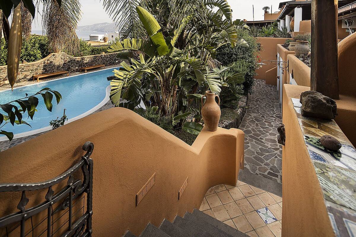 Un área de piscina con un sendero de piedra, un banco y un jarrón decorativo.