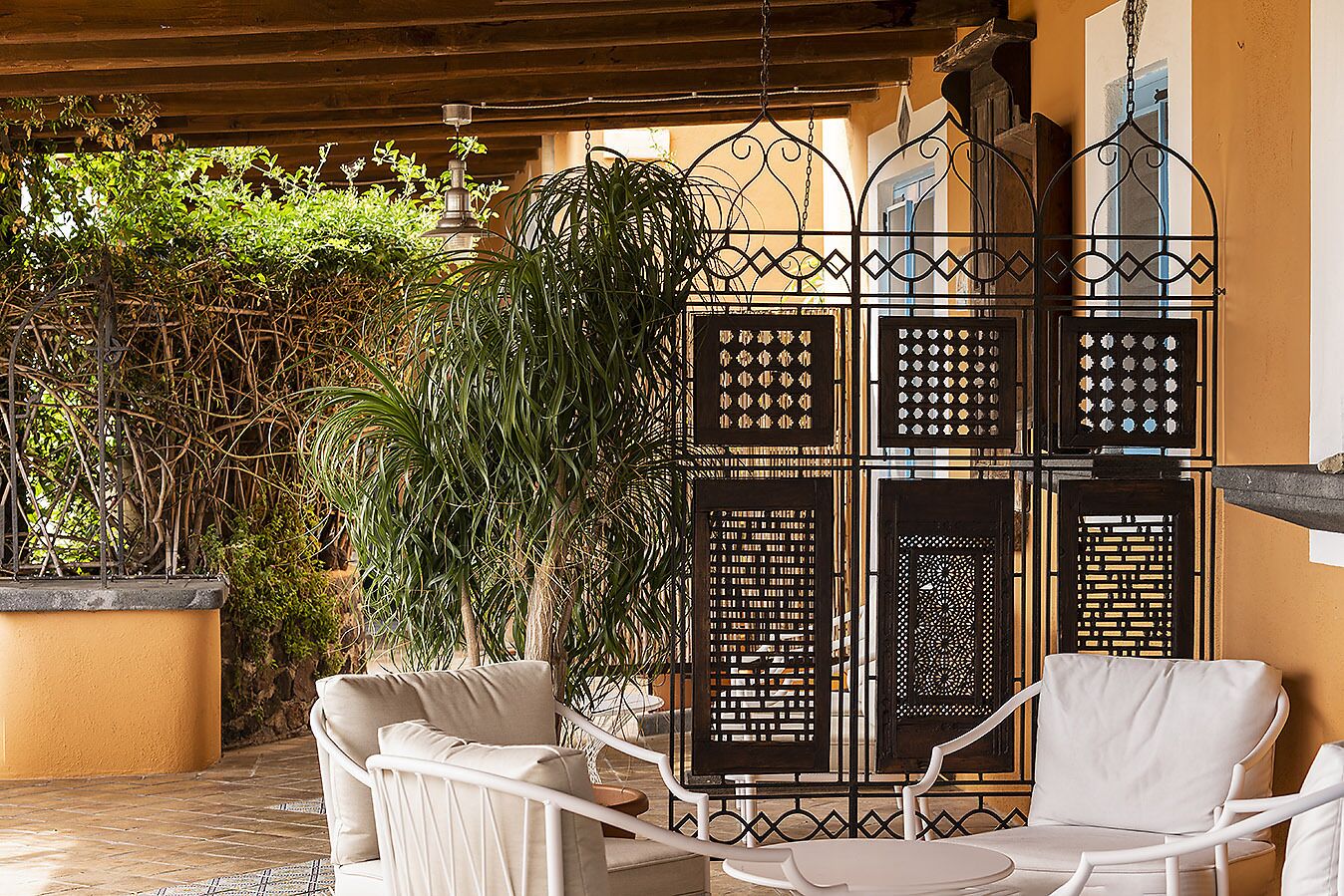 A covered outdoor seating area with white wicker chairs and a decorative metal partition.
