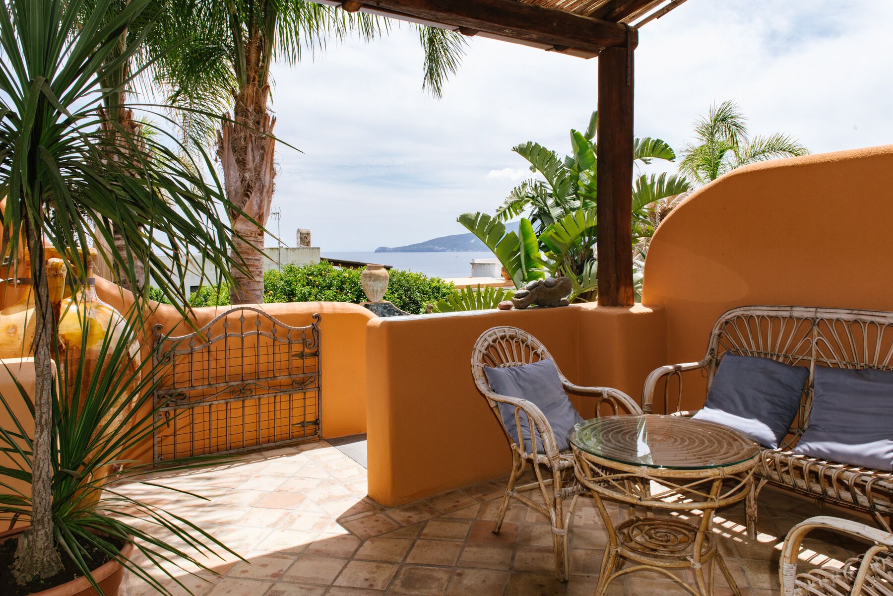 Una terraza con mobiliario de mimbre, una mesa de vidrio y vista al mar.