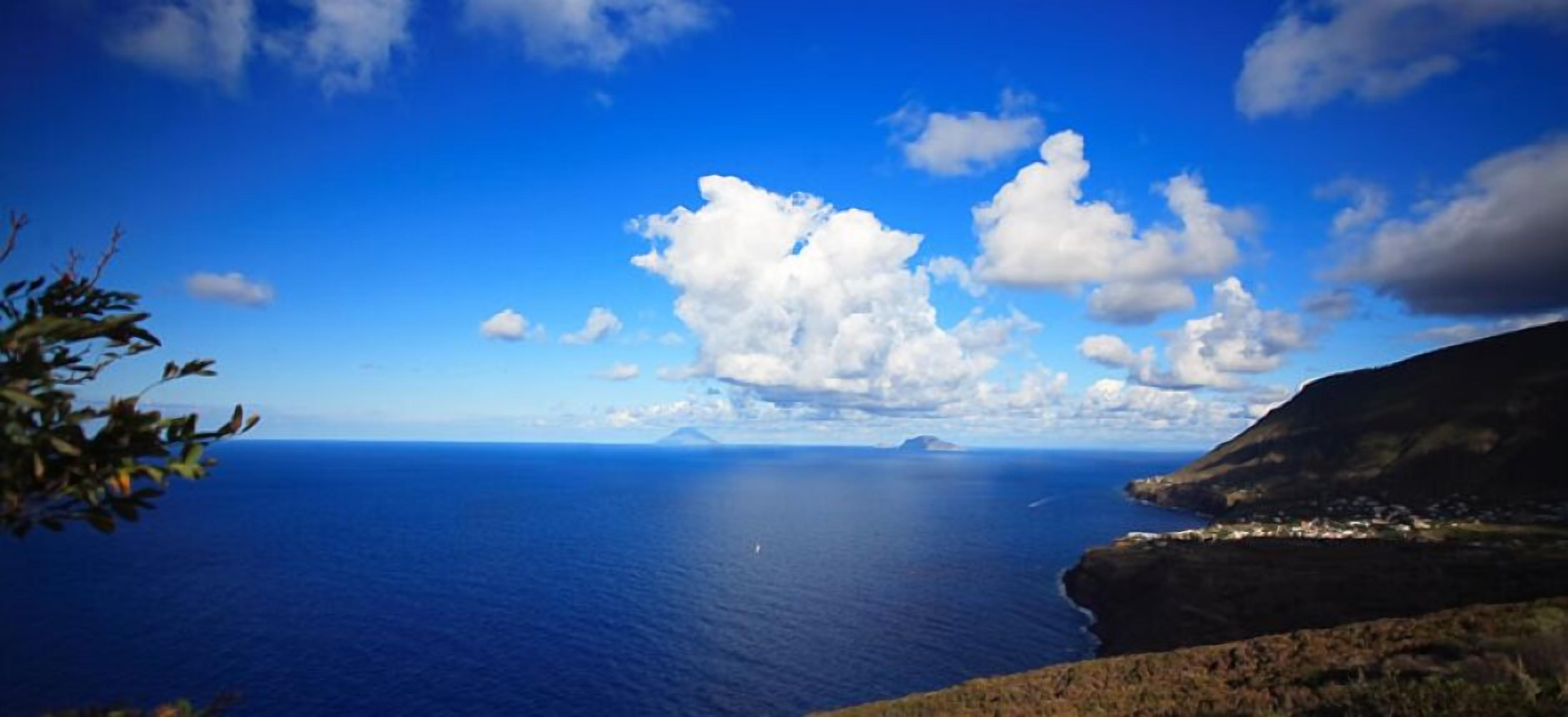 Paisaje costero con cielo despejado, vista al mar y una montaña distante.