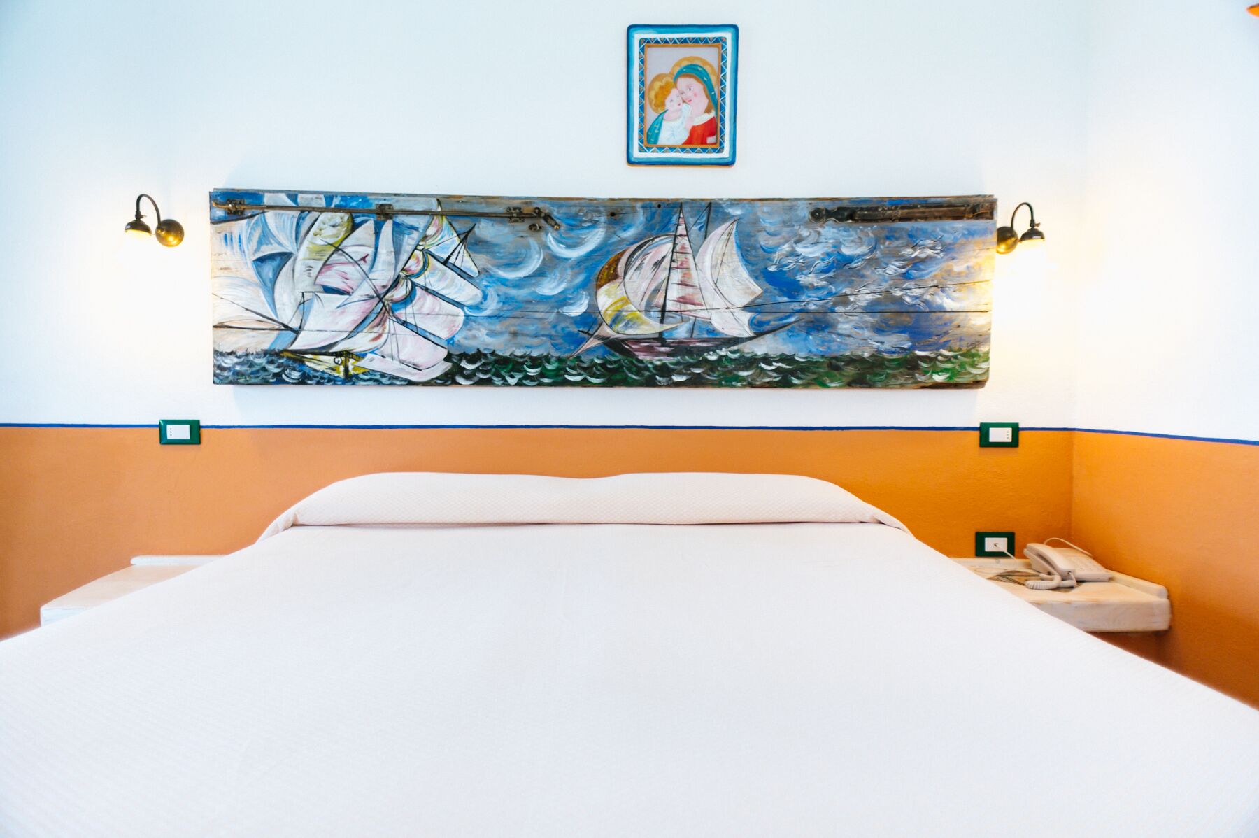 Habitación de hotel con una cama, un cuadro grande de veleros en la pared y un pequeño retrato encima del cuadro.