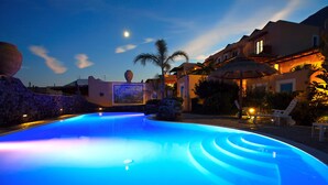 Una piscina iluminada con luz azul, rodeada de edificios y palmeras.