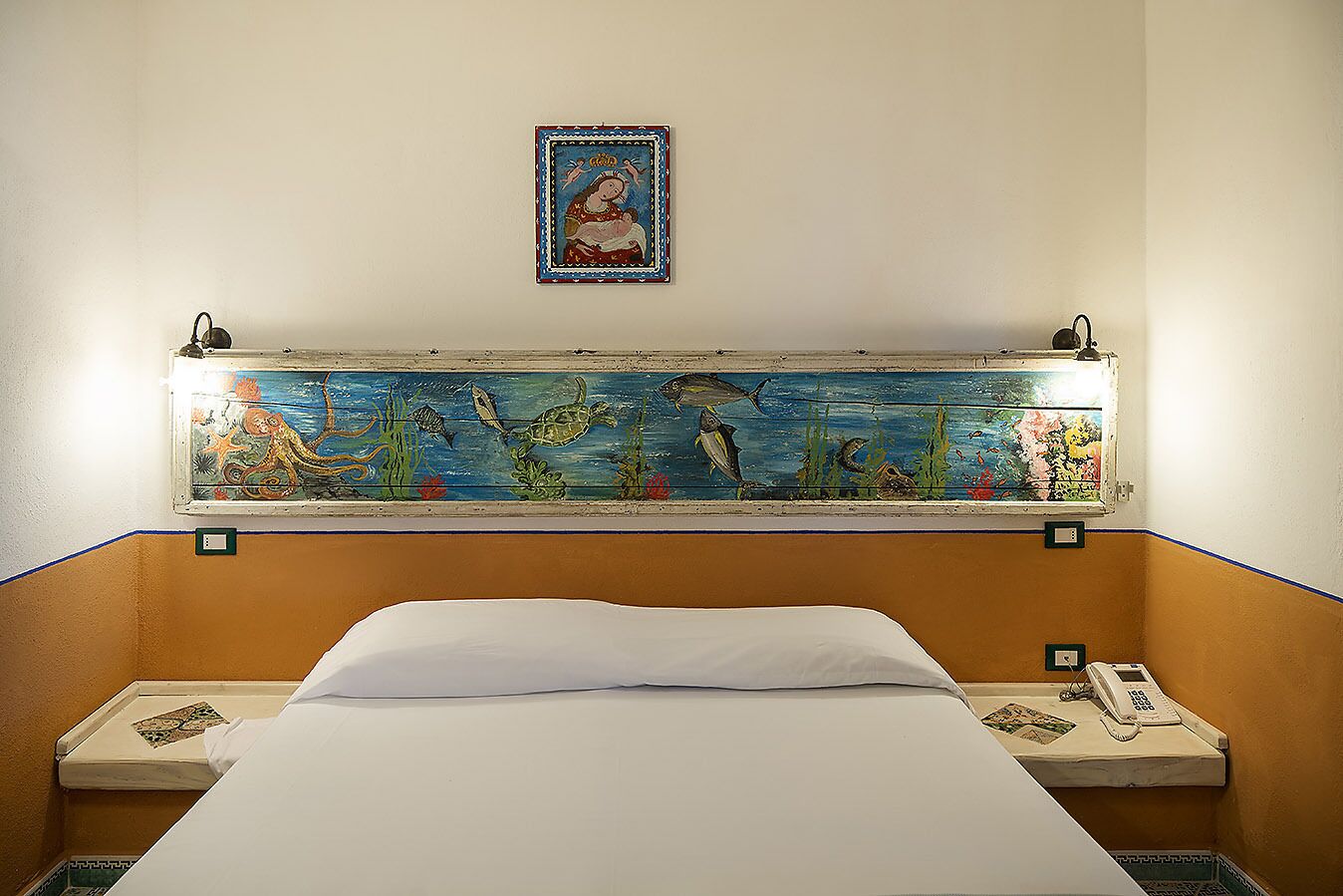 A hotel room with a bed, a nightstand with a telephone, and a wall mural depicting marine life.