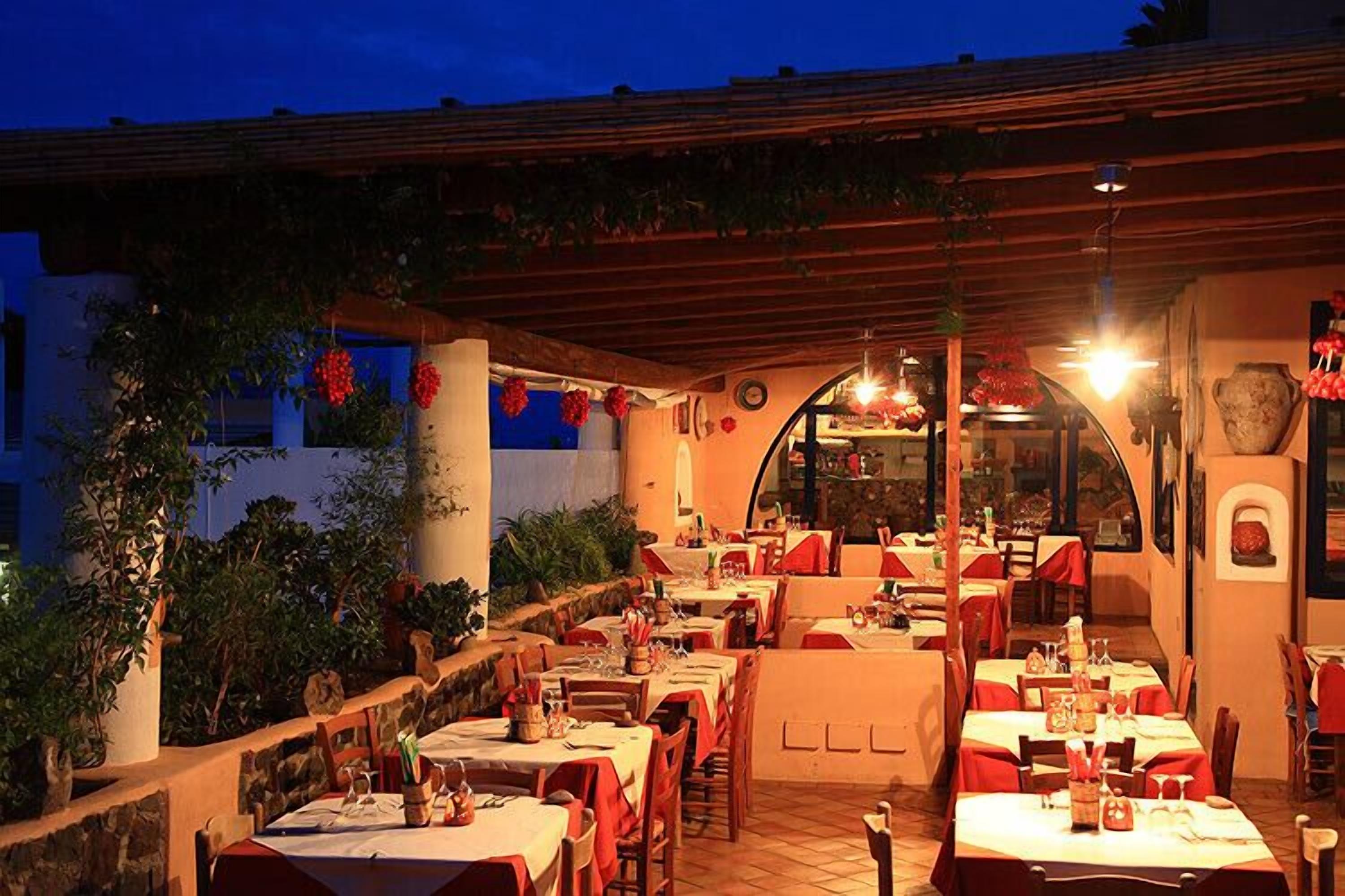 An outdoor restaurant with tables and chairs, a wooden pergola, and potted plants.