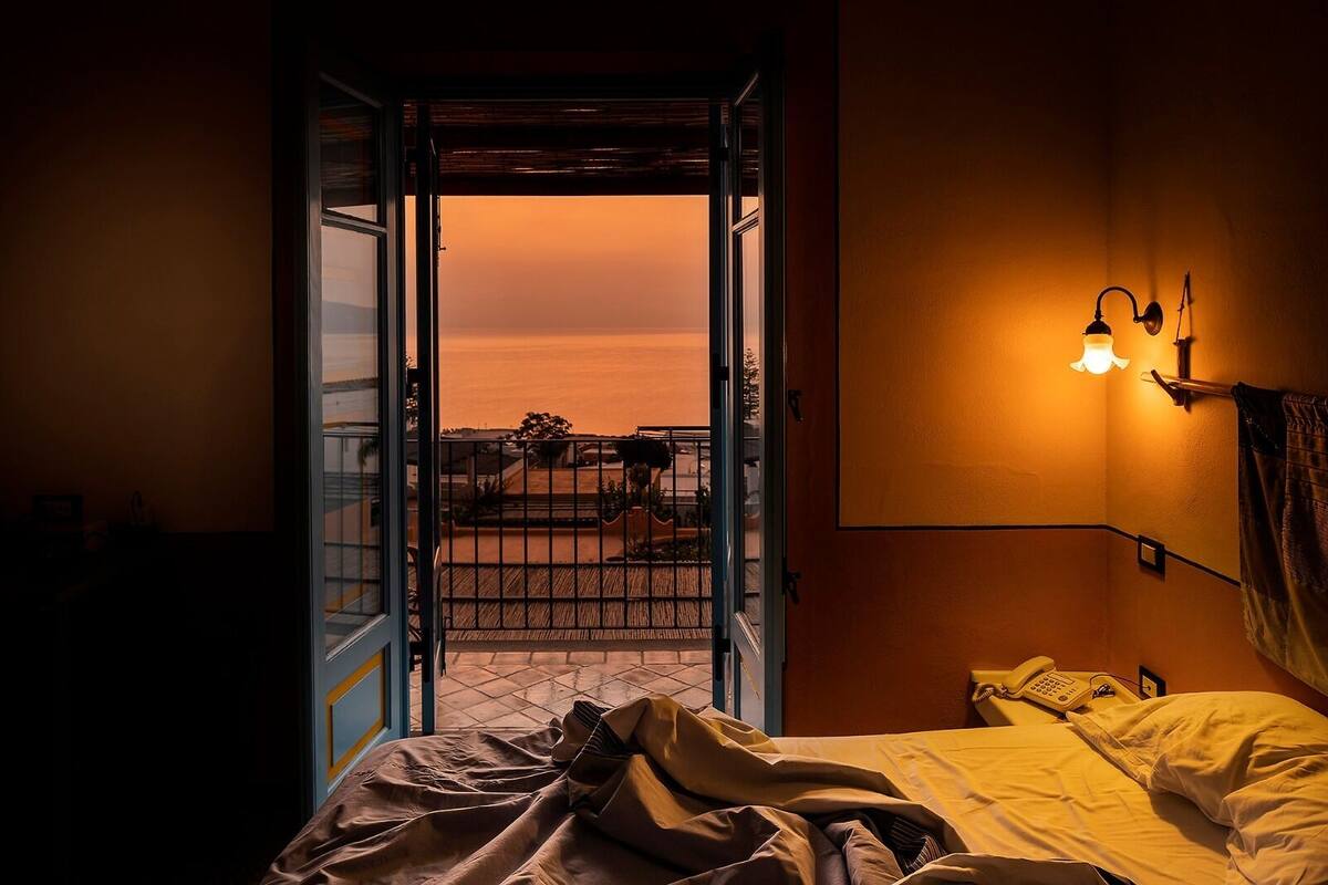 Una habitación con una cama, un teléfono en la mesita de noche y vistas a un balcón con barandilla.