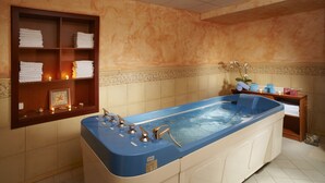 A large, blue, freestanding bathtub in a bathroom with a wooden shelf holding folded towels and a small decorative item.