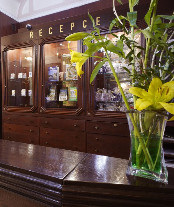 Un mostrador de recepción con acabado de madera y una vitrina de vidrio que contiene folletos y un arreglo floral amarillo.